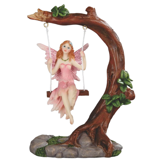 A fairy figurine sitting on a wooden swing attached to a large tree branch base, with pink wings and a pink dress, set against a plain white background.